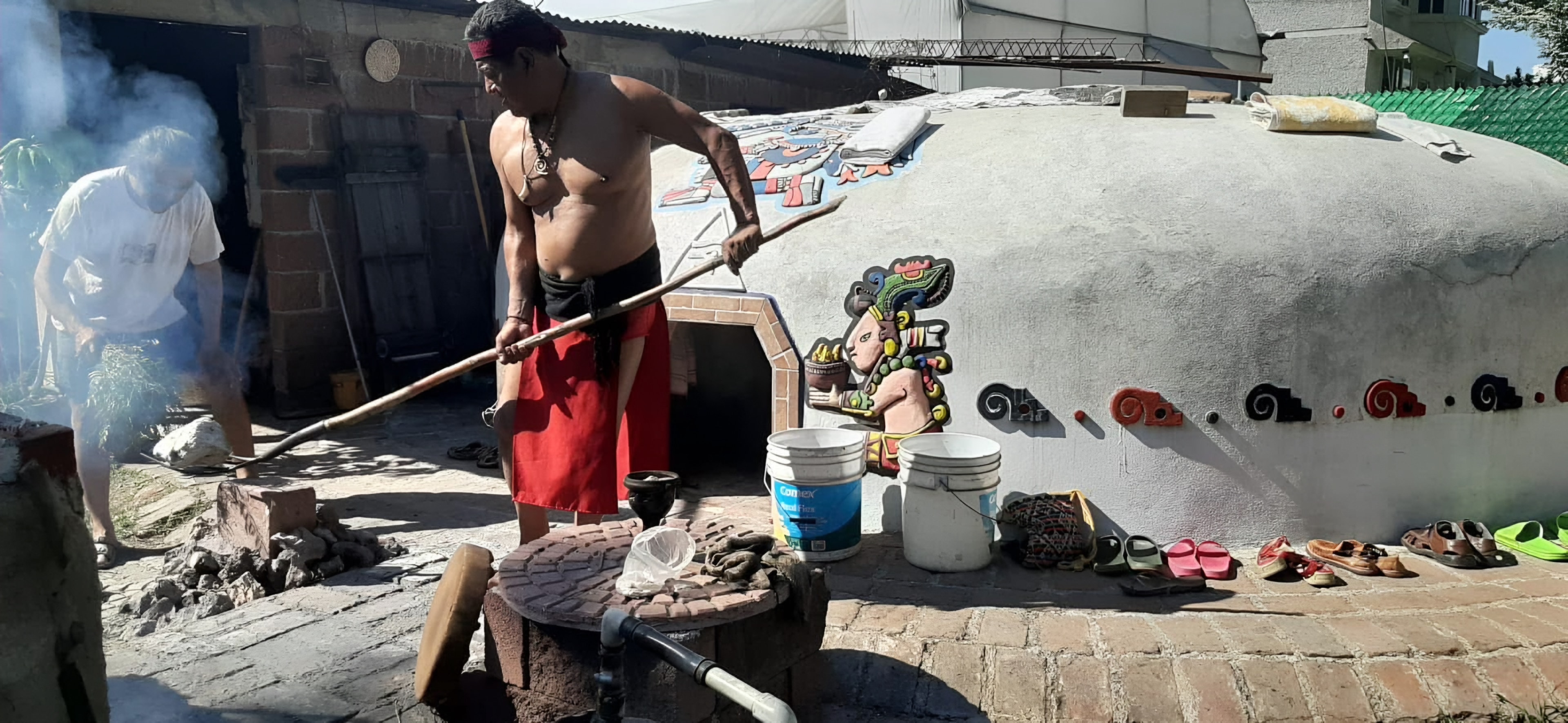 El temazcalero atizando el fuego con una vara larga junto al domo del temazcal