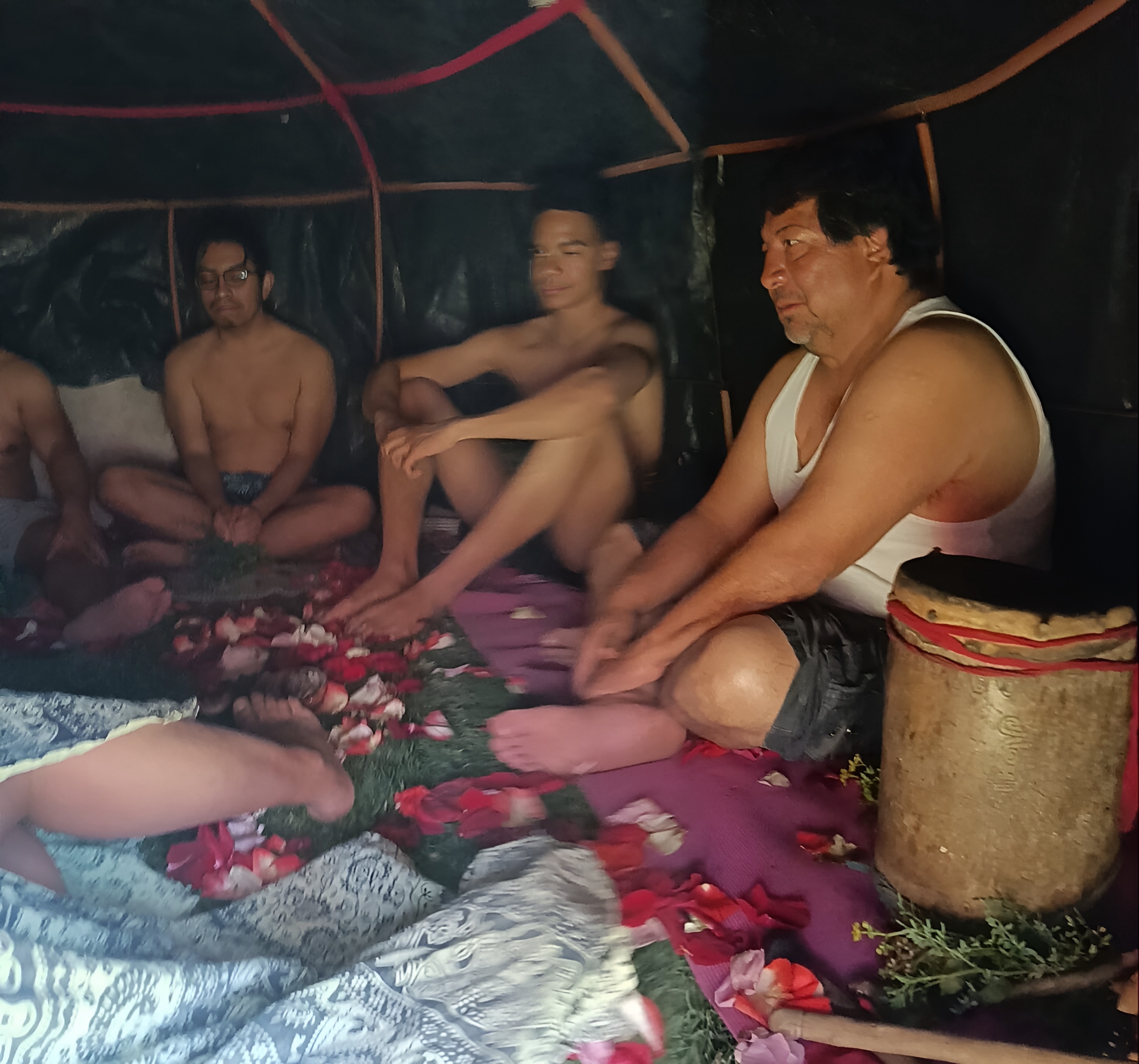 Círculo de personas sentadas sobre pétalos dentro del temazcal de campaña, con el tambor a un costado