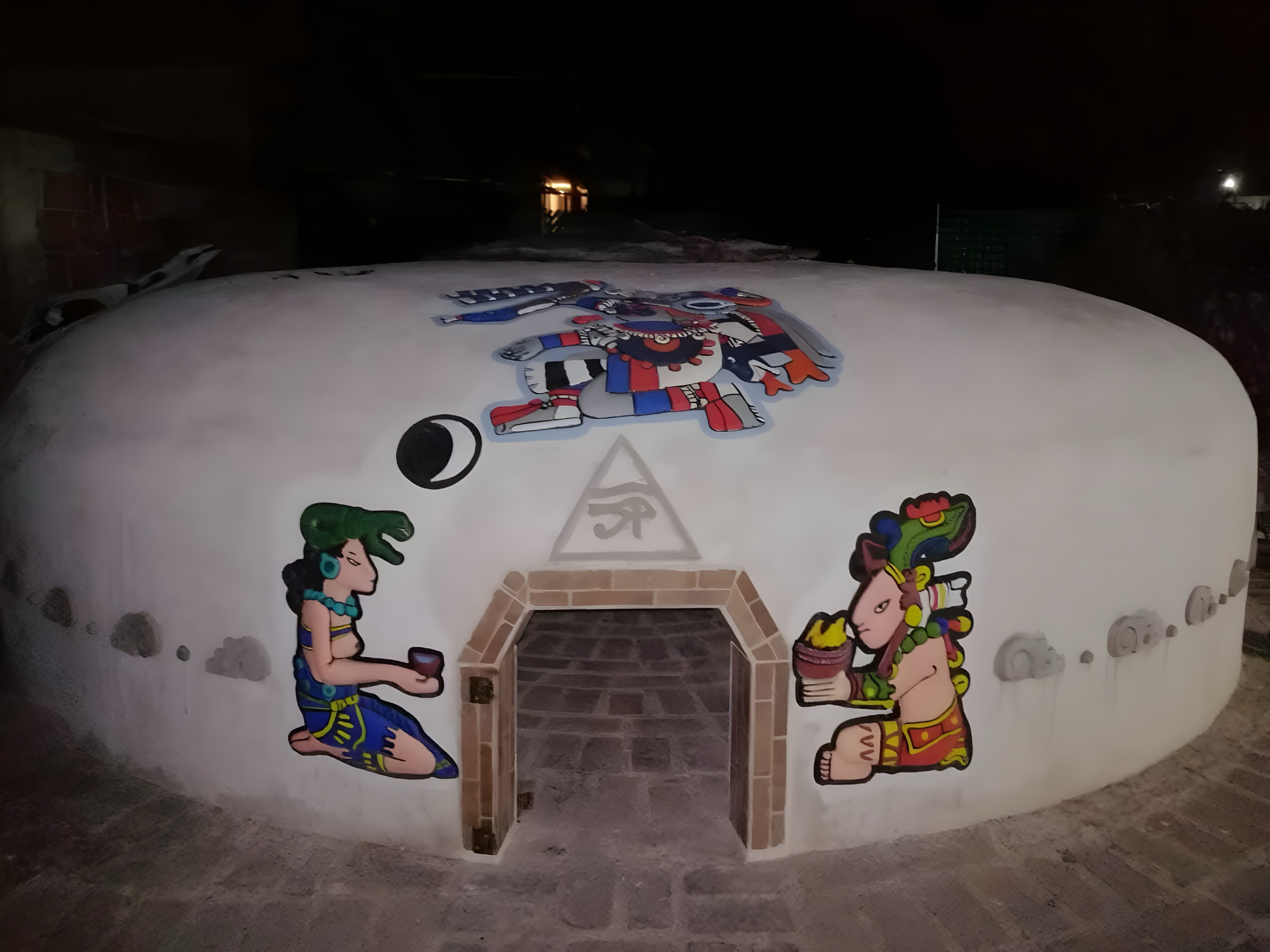 El temazcal de noche, con sus murales de figuras mesoamericanas y la entrada de ladrillo iluminada